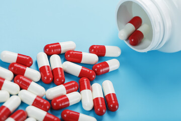 A scattering of red and white tablets capsules from a white jar on a blue background.