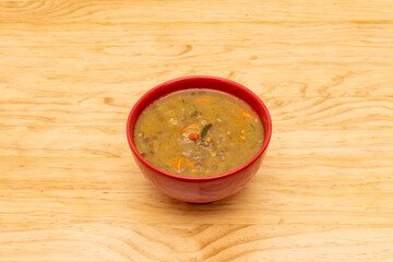 Red bowl with toasty vegan bean stew on light wood wooden table
