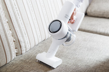 A person uses a white cordless vacuum cleaner to clean the sofa in the living room. © Alexander