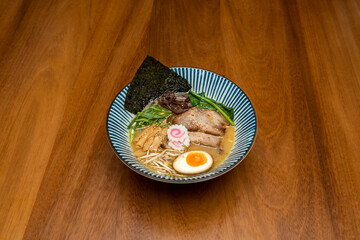 Delicious Japanese miso ramen with boiled egg, pork fillets, shiitake mushrooms, nori seaweed, noodles, bamboo and vegetables on wooden table