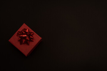 Top view of a red christmas box with a red bow on a black background with copy space for text. Black Friday and Boxing Day arrangement.