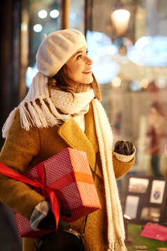 Smiling woman with Christmas present looking in shop window