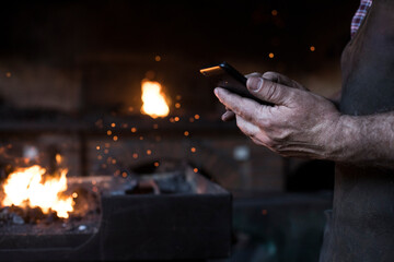 Close-up of blacksmith holding cell phone in his workshop