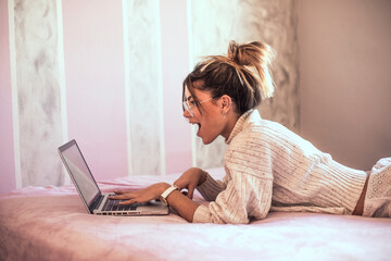 Surprised young woman lying on bed using laptop