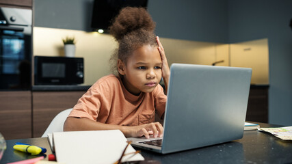 Biracial little girl doing homework at home. Kid struggling with difficult task and thinking looking at laptop screen at table. Distance education and online learning at quarantine concept - Powered by Adobe