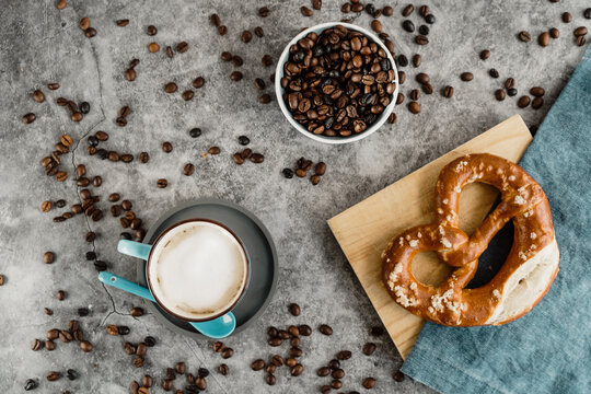 Cup of white coffee, coffee beans and pretzel on napkin and wooden board
