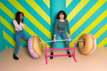 Two happy young women at an indoor theme park having fun with oversized donuts