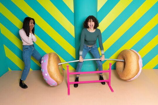 Two happy young women at an indoor theme park having fun with oversized donuts