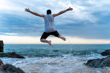 Back view of young man jumping in the air at seafront