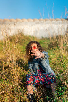 Portrait of young woman sitting on a meadow raising her hand