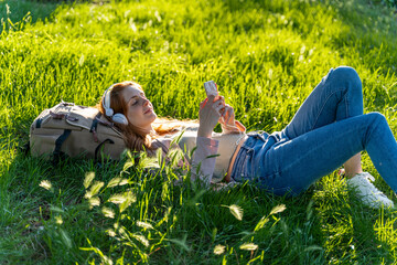 Young redheaded woman with headphones and smartphone in a park