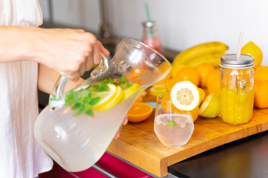 Close-up of woman in kitchen at home pouring lemonade into glass