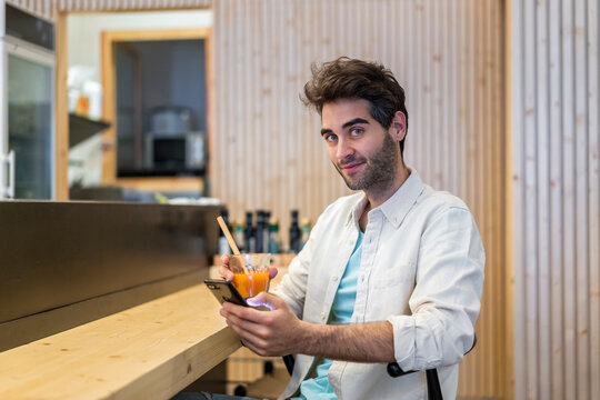 Portrait of a man with cell phone sitting at the counter of a bar having a drink