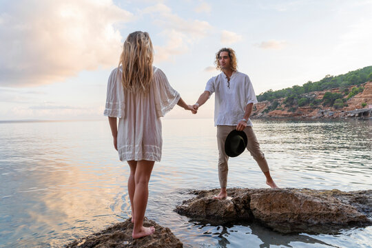 Young couple standing on rocks in front of the sea holding hands, Ibiza, Balearic Islands, Spain