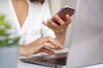 Close-up of woman using cell phone and laptop at desk