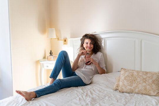 Relaxed young woman lying on bed with healthy drink