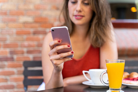 Hand of young woman at street cafe holding smartphone, close-up