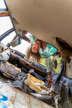 Young blond man in junk car, upside down