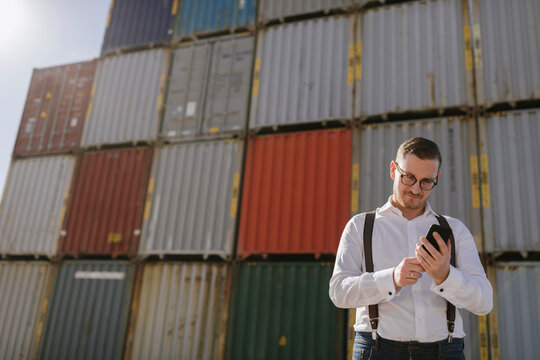 Manager in front of cargo containers on industrial site using cell phone