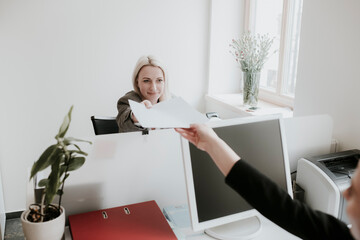 Two young women working at desk in office handing over paper