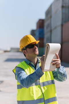 Worker with a notepad near cargo containers on industrial site