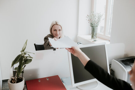 Two young women working at desk in office handing over paper