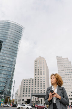 Woman holding smartphone with office buildings in background, Berlin, Germany