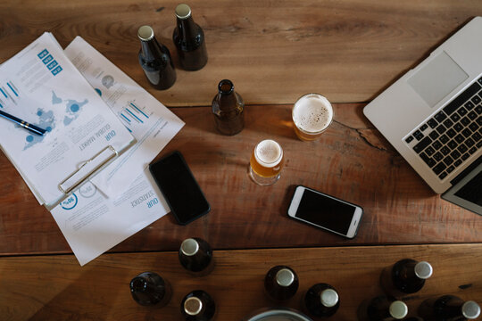 Beer bottles, glasses, documents, smartphones and laptop on table