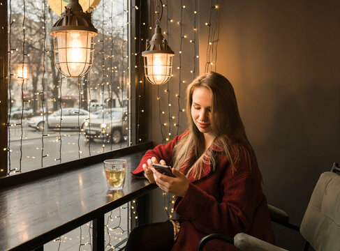 Young woman with cup of tea sitting in a coffee shop using mobile phone