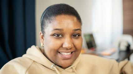 Head and shoulders portrait of beautiful Black plus size young woman in beige hoodie looking at...