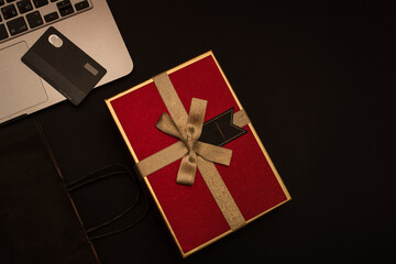 Black friday sale, laptop, red gift box, credit card and black package on red background, top view, place for text.