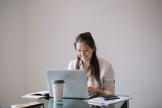 Snmiling young woman working at table in office using laptop