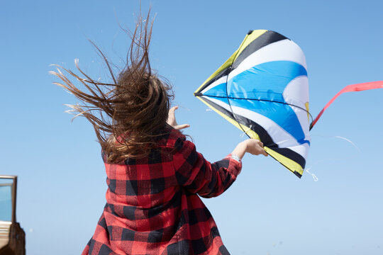 Girl with windswept hair flying kite under blue sky