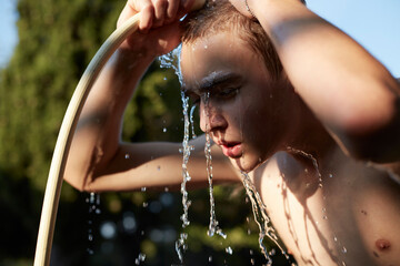 Teenage boy refreshing with water from garden hose