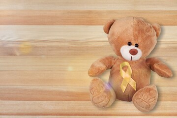 Yellow Ribbon with Bear toy on color background for supporting kid living and illness.