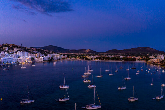 Spain, Mallorca, Santa Ponsa, Boats floating in coastal water at dusk with town in background