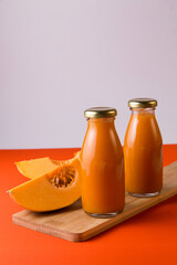 Pumpkin juice in bottles on a wooden board, background orange and white, pieces of pumpkin