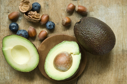 Halved avocado, blueberries and nuts on wooden table seen from above