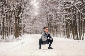 Fit sportsman crouching in nature on snow and resting from exercises. Break, healthy life, chilly weather