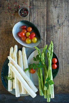 Plates and bowls with fresh cherry tomatoes, green and white asparagus, parsley, cress and pepper