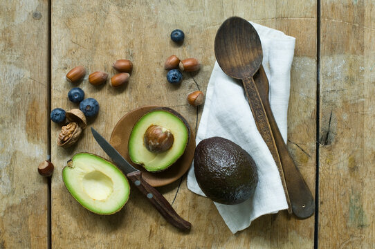 Halved avocado, blueberries and nuts on wooden table seen from above