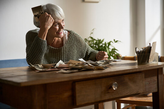 Happy senior woman sitting at table at home watching old photos