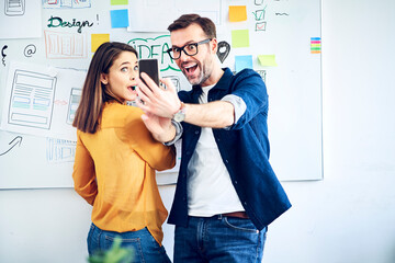 Excited colleagues looking at smartphone in office
