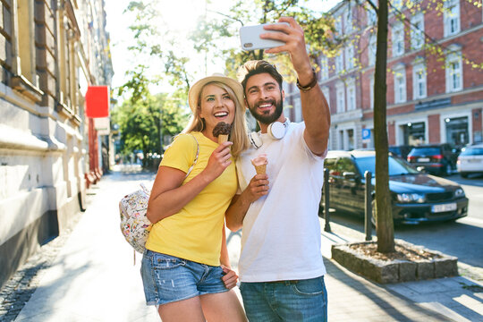 Happy young couple taking a selfie while eating ice cream in the city