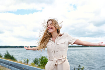 Happy woman standing at the lakeside with outstretched arms