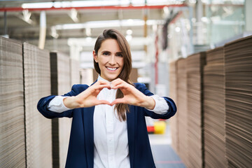 Portrait of happy businesswoman in factory warehouse shaping a heart with her hands