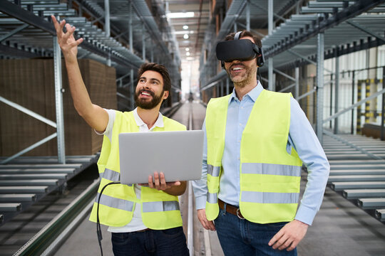 Man with laptop and businessman wearing VR glasses in factory