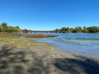 river bank with a train bridge, beach in the country, shoreline on a sunny day