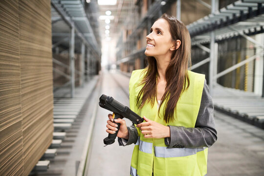 Smiling woman in factory hall wearing safety vest holding barcode scanner