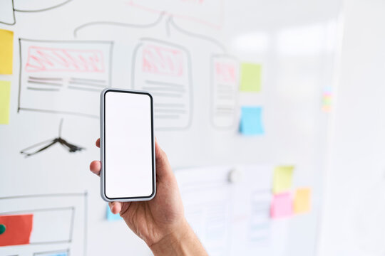 Male hand holding aloft a smartphone in front of a whiteboard